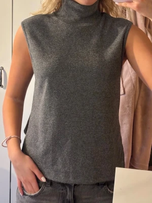 Grå ärmlös stickad poloväst - Säljer en stilren grå stickad väst med polokrage och slitsar i sidorna. Västen är ärmlös och har en rak, avslappnad passform. Jag är 180cm lång och bär vanligtvis S/M. Skicka gärna frågor eller prisförslag!