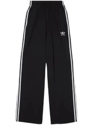 Svarta Adidas mjukisbyxor wide fit - Säljer ett par svarta mjukisbyxor från Adidas med klassiska vita ränder längs benen och broderad logga på låret. Byxorna har bred passform och elastisk midja för skön känsla. Perfekta för chill eller träning.