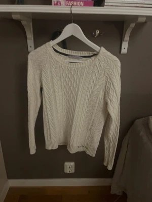 Vit kabelstickad tröja - Kabelstickad vit tröja med rund halsringning och långa ärmar. Tröjan har ett klassiskt flätmönster och ribbade muddar vid ärmslut och nederkant. 