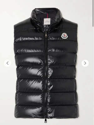 Svart dunväst från Moncler - Snygg svart dunväst från Moncler med glansig finish och klassisk quiltad design. Västen har hög krage, dragkedja framtill och Monclers ikoniska logga på bröstet. Perfekt för lager-på-lager och ger en clean look till din outfit.
