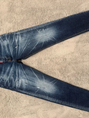 Blå jeans från dsquared  - Säljer ett par blå jeans från dsquared med snyggt slitna detaljer och ljusa tvättade partier. Jeansen har klassisk femficksmodell, silverfärgade knappar och kontrastsömmar. Perfekta för en avslappnad och trendig look.