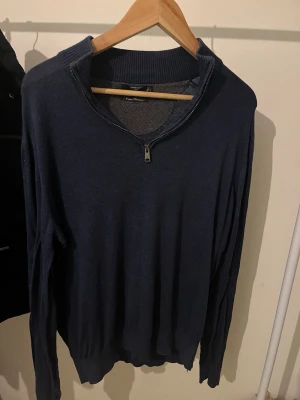 Mörkblå stickad tröja från Mango - Snygg mörkblå stickad tröja från Mango med halv dragkedja vid halsen och ribbade muddar. Perfekt för lager på lager och enkel att matcha med jeans eller chinos. Materialet känns mjukt och bekvämt mot huden. Skick 8,5/10. Lite skrynklig nedtill men går lätt att fixa med ett strykjärn på nolltid! Storlek L men skulle säga att den passar M bättre