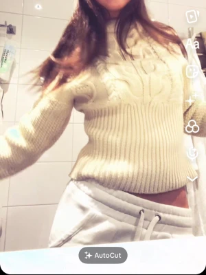 Beige kabelstickad polotröja - Säljer en beige kabelstickad polotröja med hög krage och ribbade muddar. Tröjan har ett klassiskt flätmönster framtill och är gjord i ett tjockare garn som håller dig varm. Perfekt för dig som gillar en mysig och trendig look.