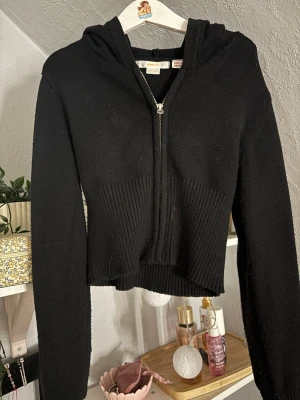 Svart cropped hoodie med dragkedja - Snygg svart hoodie från Brandy Melville med dragkedja framtill och ribbad midja. Croppad modell med huva och långa ärmar. Perfekt till jeans eller kjol för en avslappnad och trendig look.
