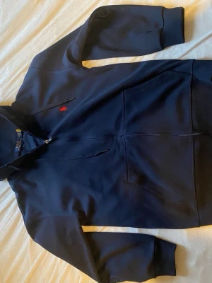  hoodie från Polo Ralph Lauren - Snygg hoodie från Polo Ralph Lauren med dragkedja framtill och klassisk röd logga broderad på bröstet. Hoodien har fickor på magen, ribbade muddar och justerbar huva. Tillverkad i mjuk bomull för skön komfort.