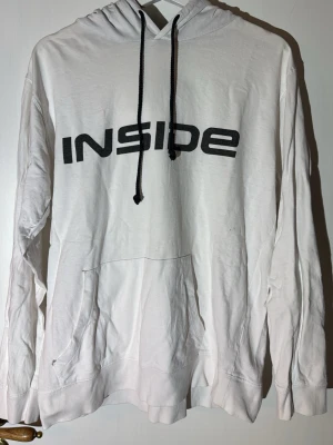 Vit hoodie från Inside med tryck - Vit hoodie från Inside med svart tryck på bröstet och svarta snören i huvan. Klassisk känguruficka framtill och mjukt material som känns skönt mot huden. Perfekt för dig som gillar en enkel men snygg stil.