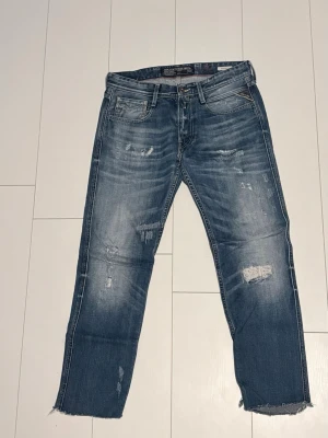 Blå Replay jeans med slitningar - Säljer ett par blå Replay jeans med slitna detaljer och råa, avklippta benslut. Jeansen har en relaxed fit. Strl 30-30 passar 172-178