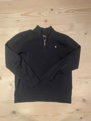 Mörkblå stickad tröja med halvzip - Snygg mörkblå stickad tröja med halvzip och ståkrage från Morris. Tröjan har ribbade muddar vid ärmslut och nederkant samt en liten broderad logga på bröstet. Perfekt för lager på lager och enkel att matcha till olika outfits. 
