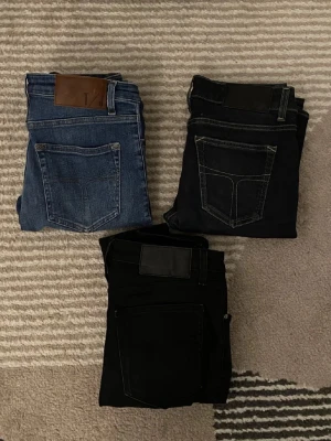 3-pack jeans blå & svarta, Shelly - Säljer ett 3-pack jeans i olika färger: ett par klassiska blå jeans och två par svarta jeans. Modellen Shelly, raka ben och normal passform. Snygga kontrastsömmar och femficksdesign. Perfekta för dig som vill ha stilrena och mångsidiga jeans i garderoben.