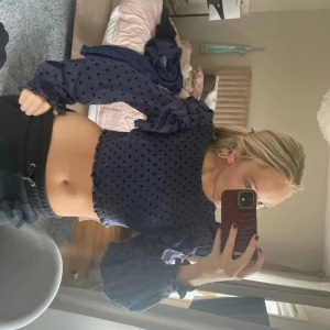 Mörkblå prickig croppad blus - Trendig mörkblå blus med transparenta, puffiga ärmar och prickigt mönster. Croppad modell med resår i midjan och vid ärmslut. Perfekt för dig som vill sticka ut lite extra.