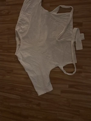 Vit tshirt med knytband från Nelly - Säljer en vit tshirt från Nelly i storlek S. Toppen har rund halsringning, långa ärmar och trendiga knytband i bak som ger en snygg detalj. Perfekt att styla till jeans eller kjol för en fräsch look.