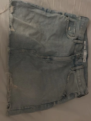 Ljusblå jeanskjol med rå kant - ljusblå jeanskjol från mango med fransig, rå kant och slitningar. Klassisk femficksmodell med bälteshällor och dragkedja fram. Perfekt för dig som gillar en avslappnad och cool stil.