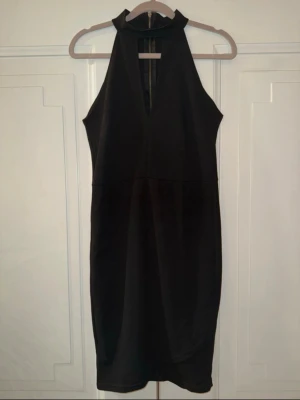 Svart ärmlös kortklänning - Snygg svart kortklänning med hög krage och djup v-ringning framtill. Klänningen är ärmlös och har en smickrande passform. Dragkedja baktill för enkel påklädning. Perfekt för dig som vill ha en stilren och modern look. Från bubbleroom by Molly Rustas