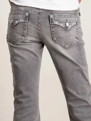 Grå bootcut jeans med mönstrade fickor - Snygga grå jeans med bootcut passform och unika bakfickor med dekorativt mönster och knappdetaljer. Jeansen har klassisk femficksdesign och är tillverkade i mjukt denimtyg som ger en avslappnad vibe. De sitter bättre men då dessa bilder är från kids brand store och inte gina tricots hemsida, hade modellen lite för stor stl.