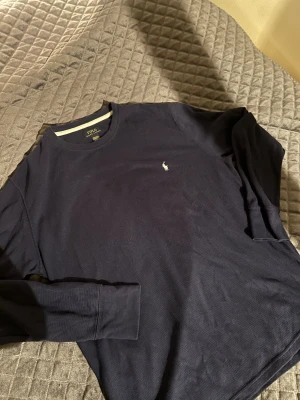 Mörkblå långärmad tröja Polo Ralph Lauren - Säljer en mörkblå långärmad tröja från Polo Ralph Lauren. Tröjan har ett diskret broderat logotyp på bröstet och är gjord i mjuk bomull med en lätt ribbad struktur. Perfekt för dig som gillar klassisk och stilren design.