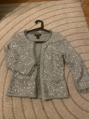 Snyggaste volang paljettkoftan❤️ - Snygg grå kofta  täckt med silvriga paljetter. Koftan har rund halsringning, två små fickor framtill och ribbade muddar och trekvartsärmad. Perfekt för dig som vill sticka ut lite extra och addera glitter till din outfit. Nyskick och passar även S . Använd gärna köp nu❤️