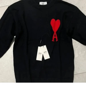 Svart stickad tröja från Ami Paris - Svart stickad tröja från Ami Paris med rund halsringning och ett stort rött hjärta. Säljer den för att den blev för stor helt o använd 