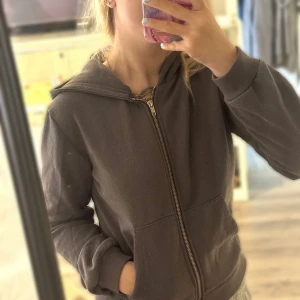 Mörkgrå hoodie från 157, storlek XS - Mysig mörkgrå hoodie från 157 med dragkedja framtill och två fickor. Tröjan har huva och är tillverkad i en mjuk blandning av bomull och polyester.