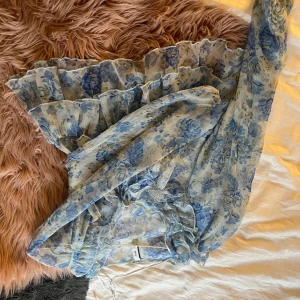Blommig volangklänning från MNG - Supersöt kortklänning från MNG med blått och beige blommönster på ljus botten. Klänningen har volanger, långärmade transparenta ärmar och snörning i midjan. Perfekt för dig som gillar romantisk och feminin stil. Den har en fin knytning fram. Använd en gång. Pris går att diskuteras💞 ny pris 429kr