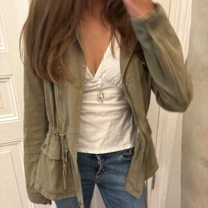 Grön jeansjacka zara  - Snygg grön jeansjacka med dragsko i midjan och stora fickor framtill. Jackan har dragkedja och knappar, samt en klassisk krage. Perfekt för lager-på-lager och enkel att styla till jeans eller kjol.