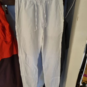 Vita linnebyxor med snörning från Akryl - Fräscha vita linnebyxor från Akryl i storlek S. De har elastisk midja med snörning och raka ben, vilket ger en chill och avslappnad vibe. Perfekta för varma dagar och enkla att matcha med sneakers eller sandaler.