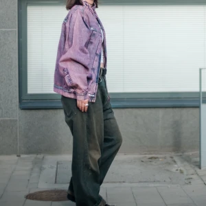 Lila oversized jeansjacka med dragkedjor - Säljer en riktigt cool lila jeansjacka i oversized modell. Jackan har en tvättad look, silverfärgade dragkedjor och knappar samt markerade sömmar. Perfekt för dig som vill sticka ut med en unik streetstyle-vibe. Passar grymt till både hoodie och crop top.