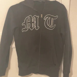 Svart hoodie från TUTTOLENTE - Svart hoodie med stor vit tuttolentes tryck på bröstet och en mörk, diskret örn på ryggen. Tröjan har huva, dragkedja och två fickor framtill. Perfekt för dig som gillar streetwear och vill ha en cool look. Kom privat för funderingar