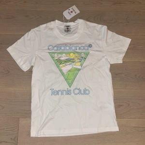 Casablanca Tennis Club t-shirt vit - Vit t-shirt från Casablanca med färggrafiskt tryck och texten 'Tennis Club' på framsidan. Klassisk rund hals och korta ärmar. Materialet är mjuk bomull och passformen är normal. Perfekt för dig som gillar sportig och clean stil.
