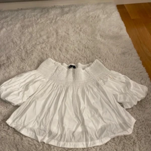 Vit offshoulder blus från Zara - Säljer en vit blus från Zara i storlek XS med offshoulder och puffiga korta ärmar. Blusen har smock upptill och är gjord i mjuk bomull. Perfekt för dig som gillar en luftig och trendig stil med snygg passform.