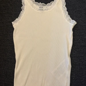 Vit ribbad linnetopp från ONLY - Säljer en vit ribbad linnetopp från ONLY i storlek S. Toppen har fina spetsdetaljer runt halsringningen och axlarna, vilket ger en romantisk vibe. Materialet är mjukt och stretchigt, perfekt för varma dagar. Snygg att styla med jeans eller kjol!