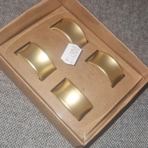 Servettringar - Fyra stilrena servettringar i guldfärgad metall från Form Living. De har en mjukt böjd form med små dekorativa kulor längs kanterna. Perfekta för att ge dukningen en lyxig touch. Levereras helt nya, i originalförpackning.