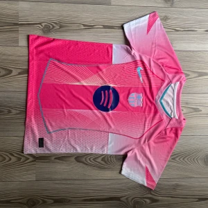 Rosa FC Barcelona Nike fotbollströja - Snygg FC Barcelona fotbollströja från Nike i olika rosa nyanser med vita detaljer. Tröjan har korta ärmar, klubbmärke och Nike-logga på bröstet samt ett stort blått Spotify-tryck i mitten. Tillverkad i lätt och ventilerande material.