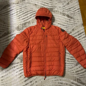 Orange dunjacka från Parajumpers - Säljer en orange dunjacka från Parajumpers med huva och klassisk patch på ärmen. Jackan har dragkedja framtill, två sidofickor med dragkedja och en bröstficka. Insidan är ljusbeige och jackan är quiltad för extra värme. Perfekt för kalla dagar.ny pris 4500kr. Pris kan diskuteras 