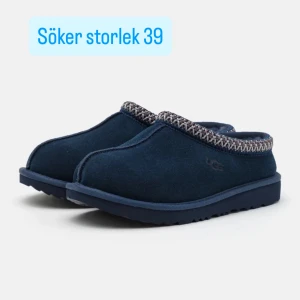 SÖKER Mörkblå slip-in skor från UGG - Söker i storlek 39. Mörkblå slip-in skor från UGG i mocka med rund tå och platt sula. Skorna har dekorativt mönsterband runt öppningen och är perfekta för kalla dagar. Klassisk UGG-logga på sidan och mjuk insida för extra komfort.