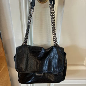 Axelväska med kedja från Zara  - Bra skick, lite sönder i ytterfacket men går att sy ihop! Svart axelväska i skinn med quiltat mönster och kedjerem. Väskan har ett lock med metallspänne och fyra fack inuti, ett med dragkedja. 