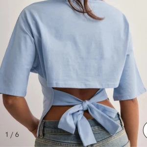 Ljusblå croppad topp med knyt - Säljer en ljusblå croppad topp med korta ärmar och snygg öppen rygg med knyt i midjan. Toppen har en enkel, stilren design och är tillverkad i mjukt bomullsmaterial. Perfekt för dig som gillar trendiga detaljer och vill ha en chill look.
