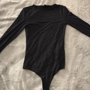 Svart långärmad body från Amisu XS - Svart, stilren långärmad body från Amisu i storlek XS. Gjord i ett mjukt och stretchigt syntetmaterial som sitter tight mot kroppen. Aldrig använd 💕