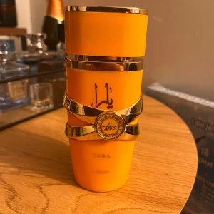 Yara Lattafa - Snygg och trendig parfym i orange flaska med guldiga detaljer. Märkt med 'Yara' och Lattafa. Perfekt för dig som vill sticka ut med din doftsamling.