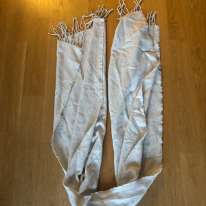 Beige halsduk med fransar - Snygg och enkel beige halsduk med fransar i ändarna. Halsduken är lång och har en mjuk, slät yta som gör den skön att bära. Perfekt att svepa runt halsen för extra värme och stil. Passar till de flesta jackor och outfits. Helt oanvänd!💞