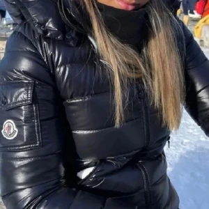 Svart pufferjacka från Moncler - Säljer en svart pufferjacka från Moncler med glansig finish och huva. Jackan har dragkedja framtill, ficka med knapp på ärmen och klassisk Moncler-logga. Perfekt för kalla dagar och riktigt snygg streetstil.