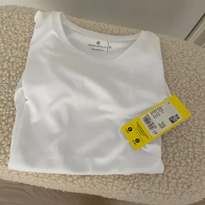 Vit sportig t-shirt från Ronhill XS - Fräsch vit t-shirt från Ronhill i sportig modell. Tillverkad i lätt och mjuk polyester som andas, perfekt för träning. Klassisk rund halsringning och korta ärmar. Enkel och stilren design utan mönster eller tryck. Helt ny! Aldrig använd! Nypris 180 