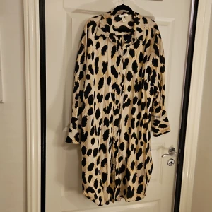Leopardmönstrad lång skjortklänning H&M - Lång skjortklänning från H&M med leopardmönster i svart och beige. 100% bomull.Klänningen har klassisk krage, knappar framtill och långa ärmar.