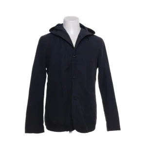 Mörkblå jacka med huva från Massimo Dutti - Stilren mörkblå jacka från Massimo Dutti med huva och knäppning framtill. Jackan har en klassisk passform och påminner lite av en windbreaker. Perfekt för dig som gillar en clean look med snygga detaljer. Jackan saknar en knapp, dock inget man lägger märke till. 