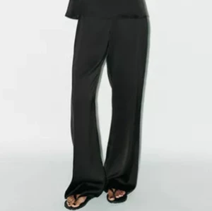 Svarta vida satinbyxor - Snygga svarta byxor med vid passform och hög midja i glansigt satinmaterial. Byxorna har raka ben och en stilren look som ger en lyxig känsla. Aldrig använda men har inte lappen kvar tyvärr. Köpta för 379kr.