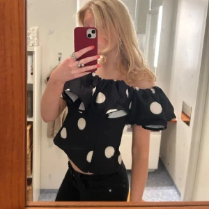 Svart prickig offshoulder topp - Säljer en svart offshoulder topp med stora vita prickar och bred volang runt axlarna. Super fin men kommer tyvärr inte till användning😇🩵