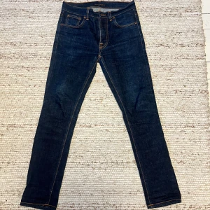 Mörkblå Raw Lean Dean jeans från Nudie  - Snygga mörkblå Lean Dean jeans från Nudie Jeans med klassisk femficksdesign och orangea sömmar. Modellen är slim och har raka ben, tillverkad av 98% ekologisk bomull och 2% elastan för extra stretch. Perfekt passform och stilren look. Nyskick skicka vid minsta fråga säljer på grund av fel storlek för mig 👍