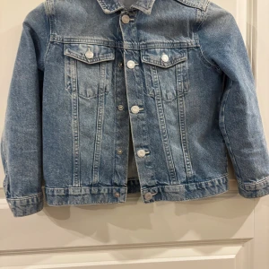 Klassisk blå jeansjacka från H&M - Snygg blå jeansjacka från H&M med klassisk passform. Jackan har silverfärgade knappar framtill, två bröstfickor med lock och knapp samt raka sömmar. Tillverkad i slitstarkt denimtyg som ger en cool och tidlös look. Pris kan diskuteras!