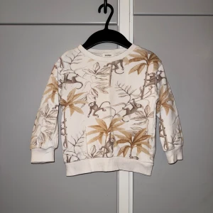 Beige sweatshirt med apor från Newbie - Superfin beige sweatshirt från Newbie med brunt och ljusbrunt djungelmönster och apor. Tröjan har rund hals, muddar vid ärmslut och nederkant samt lång ärm. Perfekt för dig som gillar lekfulla prints och mjuka material. Storlek 86/92