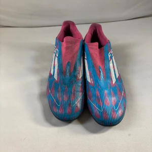Adidas F50 blå/rosa fotbollsskor - Säljer ett par Adidas F50 fotbollsskor i en riktigt snygg blå och rosa färgkombination med vita detaljer. Skorna har ett mönstrat yttre och är designade för att ge bra grepp på planen. Perfekta för dig som vill sticka ut på matchen!