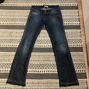 Jeans från Lee - Snygga blå jeans från Lee med klassisk femficksdesign och en bootcut modell. Jeansen har tydliga slitningar och kontrastsömmar, samt dubbla knappar i midjan.